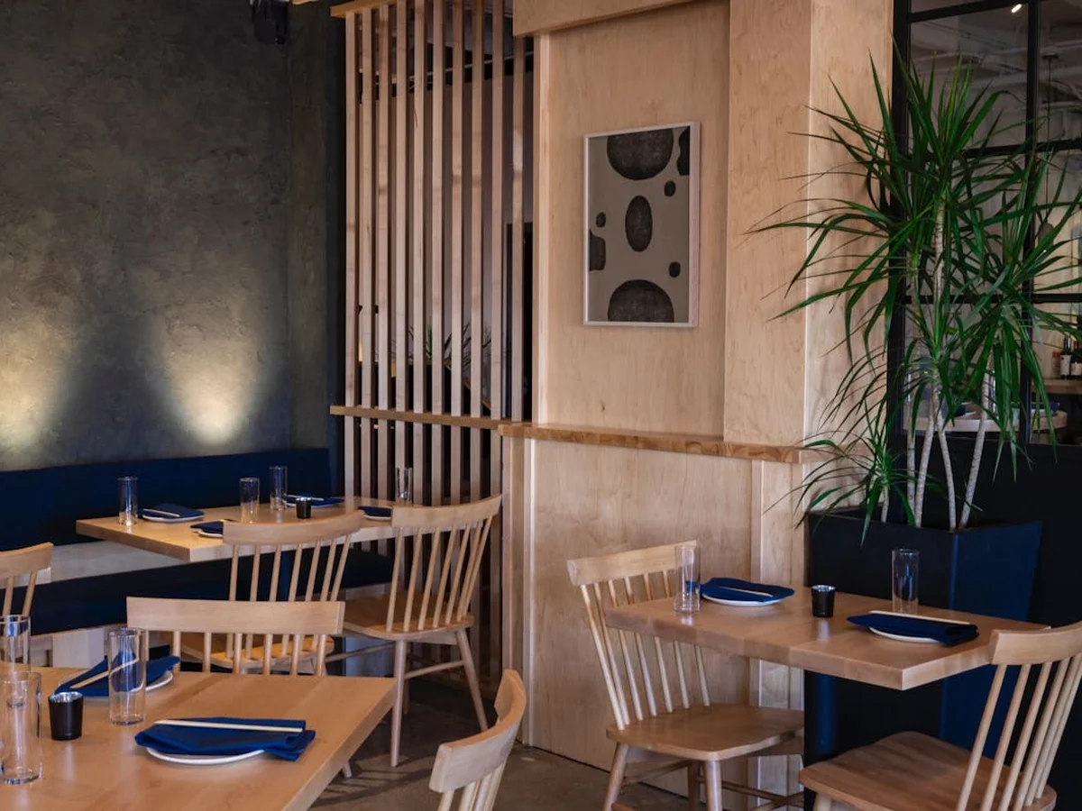 Noko’s dining room with light wood furniture, blue seating, and a leafy plant.